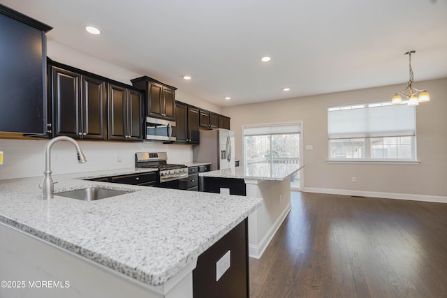 kitchen featuring a sink, dark wood-style flooring, appliances with stainless steel finishes, light stone countertops, and a kitchen island