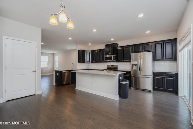 kitchen with dark wood finished floors, a center island, appliances with stainless steel finishes, a sink, and backsplash