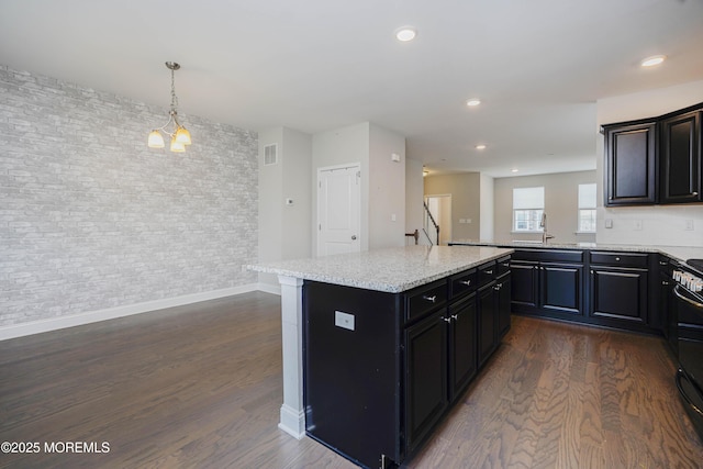 kitchen featuring dark cabinets, dark wood-style flooring, a kitchen island, visible vents, and a sink