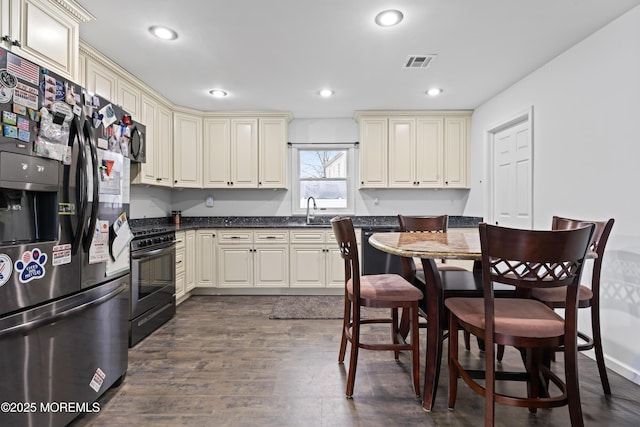 71 6th St, Belford, NJ 07718 - kitchen with cream cabinets, dark countertops, stainless steel refrigerator with ice dispenser, visible vents, and black gas range