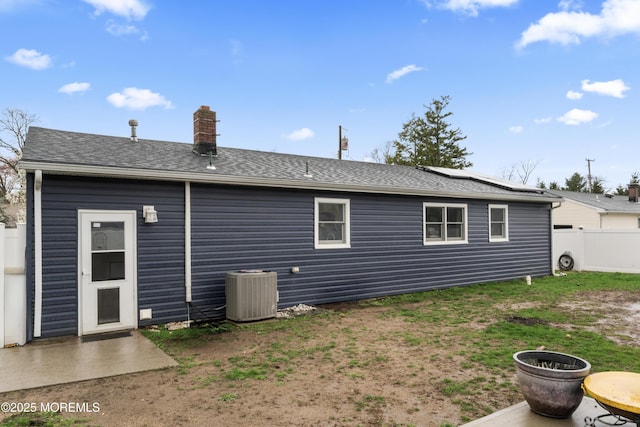 71 6th St, Belford, NJ 07718 - back of house with fence, solar panels, a chimney, a shingled roof, and central AC unit