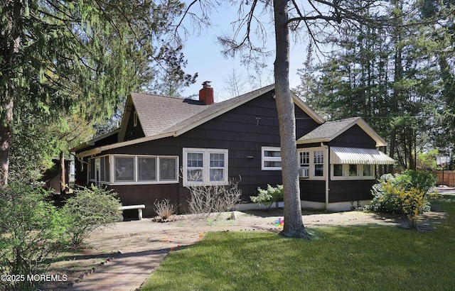 rear view of house featuring a yard, a chimney, and roof with shingles