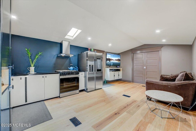 kitchen with light wood-style floors, lofted ceiling with skylight, wall chimney exhaust hood, gas stove, and stainless steel fridge with ice dispenser