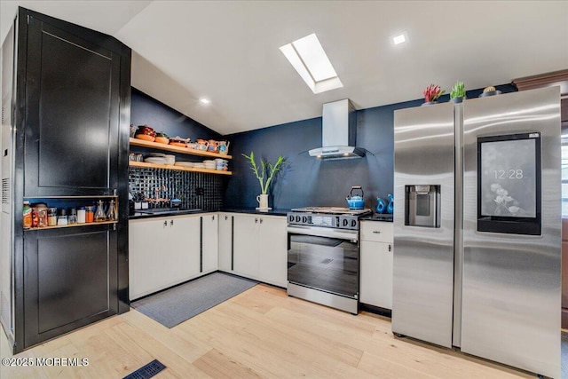 kitchen featuring wall chimney exhaust hood, dark countertops, vaulted ceiling with skylight, and range with gas cooktop