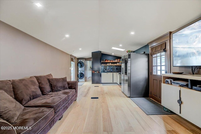living room featuring light wood finished floors, recessed lighting, vaulted ceiling, stacked washer and dryer, and a dry bar