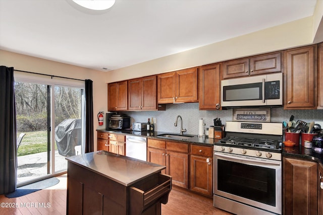kitchen featuring light wood-style flooring, dark countertops, decorative backsplash, stainless steel appliances, and a sink