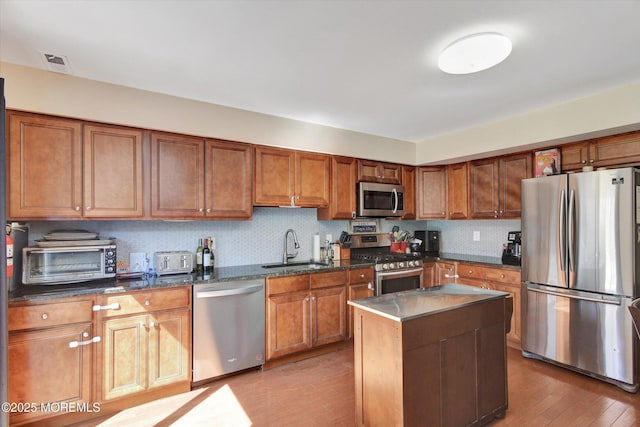 kitchen featuring brown cabinetry, light wood-type flooring, visible vents, appliances with stainless steel finishes, and a sink