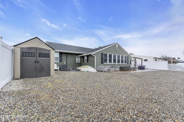 rear view of property featuring a patio, roof with shingles, a storage shed, a fenced backyard, and an outbuilding