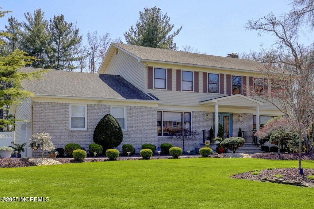 colonial inspired home featuring roof with shingles, a front yard, and brick siding