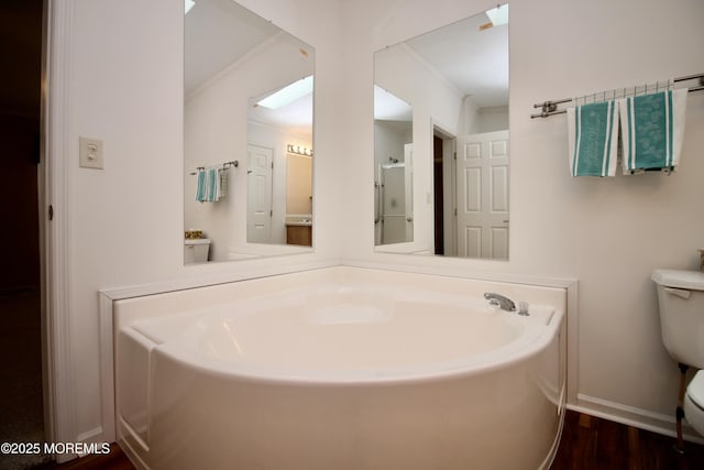 bathroom with baseboards, a bath, toilet, crown molding, and wood finished floors