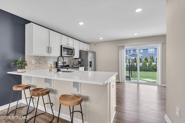 kitchen with tasteful backsplash, a breakfast bar, stainless steel appliances, wood-type flooring, and baseboards