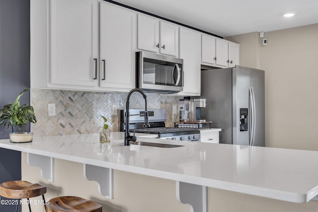 kitchen with a breakfast bar, a peninsula, tasteful backsplash, appliances with stainless steel finishes, and white cabinetry