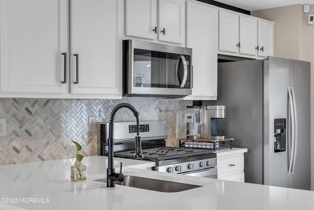 kitchen featuring white cabinets, light stone counters, a sink, tasteful backsplash, and appliances with stainless steel finishes