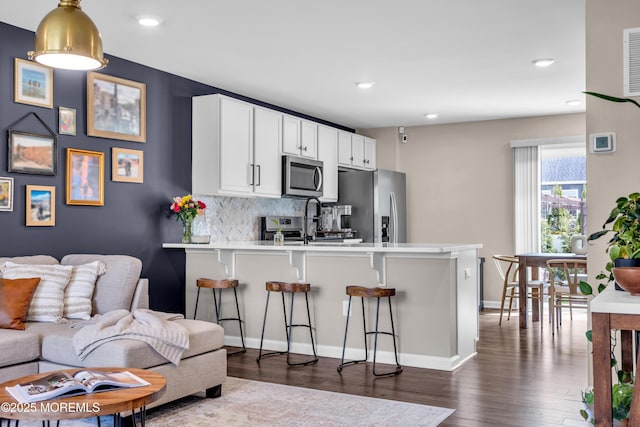 kitchen with stainless steel appliances, a peninsula, dark wood-style flooring, decorative backsplash, and a breakfast bar