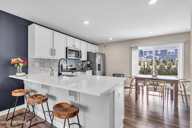 kitchen featuring stainless steel appliances, baseboards, a kitchen bar, decorative backsplash, and wood finished floors