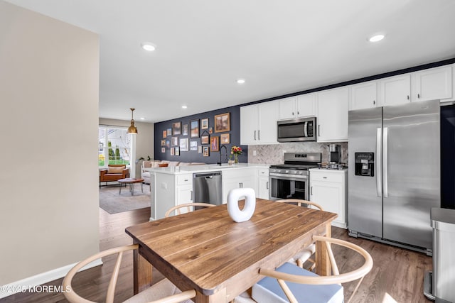 kitchen with a peninsula, wood finished floors, stainless steel appliances, and a sink