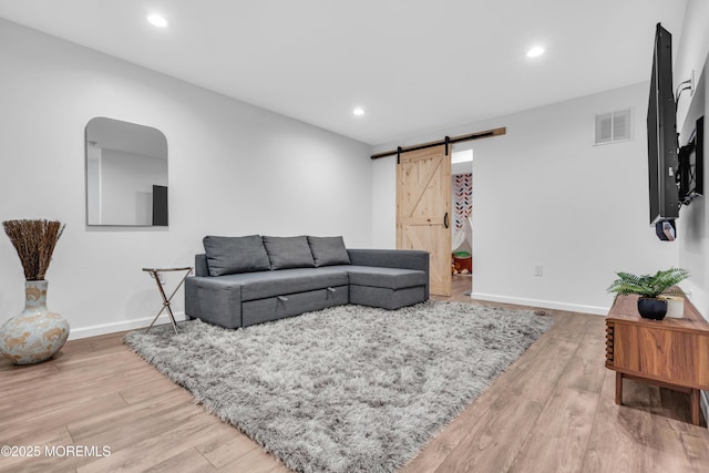 living room with a barn door, recessed lighting, visible vents, and light wood-style flooring
