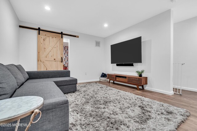 living area featuring a barn door, baseboards, wood finished floors, and visible vents