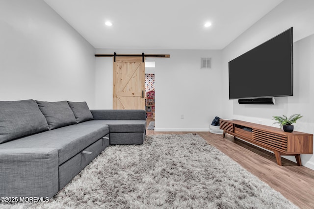 living room featuring a barn door, wood finished floors, visible vents, and baseboards
