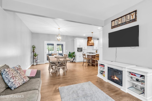 living room with a glass covered fireplace, baseboards, an inviting chandelier, recessed lighting, and light wood-style floors