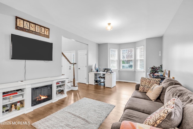 living room with a glass covered fireplace, stairs, baseboards, and wood finished floors