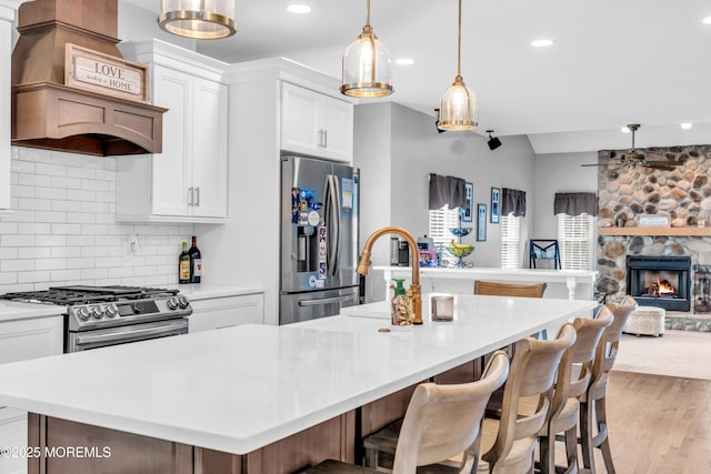 kitchen with open floor plan, a ceiling fan, backsplash, a center island with sink, and appliances with stainless steel finishes