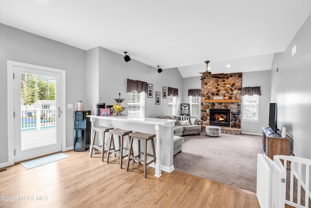 kitchen with baseboards, a stone fireplace, a ceiling fan, a peninsula, and light wood-style floors
