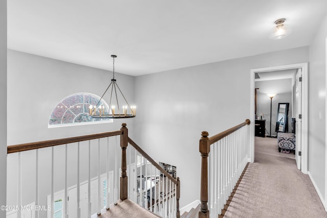 hall with a chandelier, carpet flooring, baseboards, and an upstairs landing
