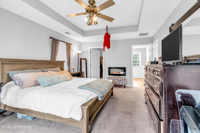 bedroom with light carpet, visible vents, ceiling fan, and a raised ceiling