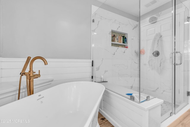 full bath with wood finished floors, a marble finish shower, wainscoting, and visible vents