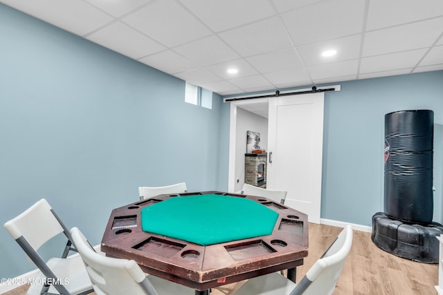 recreation room featuring a paneled ceiling, wood finished floors, baseboards, and a barn door