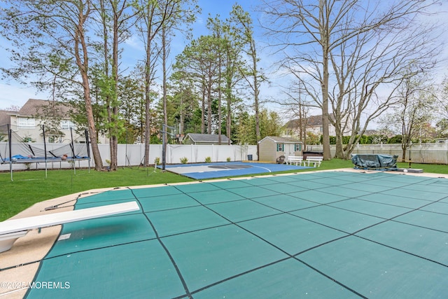 view of pool with a trampoline, a yard, a fenced backyard, and an outbuilding