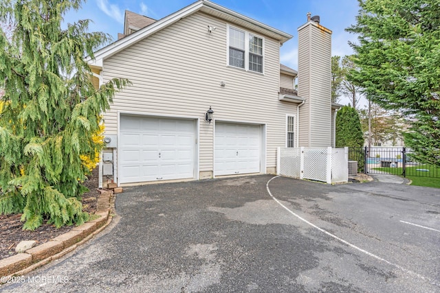 view of property exterior featuring central AC, an attached garage, a chimney, aphalt driveway, and fence