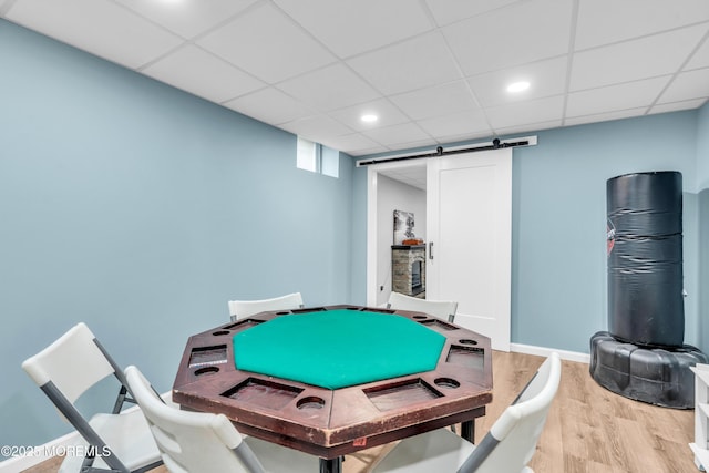 recreation room featuring a drop ceiling, recessed lighting, a barn door, wood finished floors, and baseboards