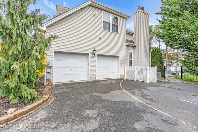 view of side of property featuring a chimney, an attached garage, aphalt driveway, central AC unit, and fence