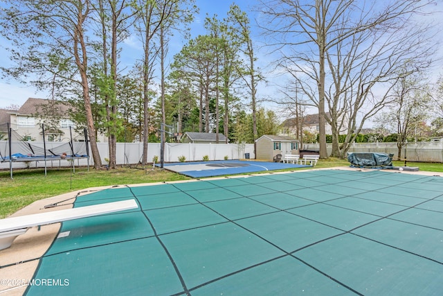 view of swimming pool featuring a trampoline, a fenced backyard, an outdoor structure, and a lawn