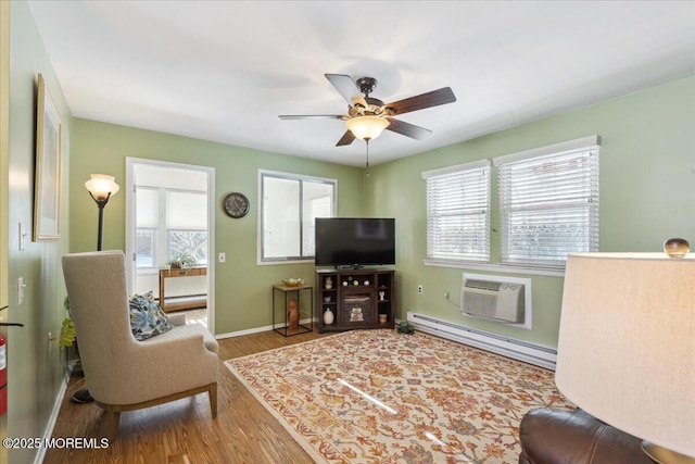 living area with a wall mounted air conditioner, baseboard heating, baseboards, wood finished floors, and a ceiling fan