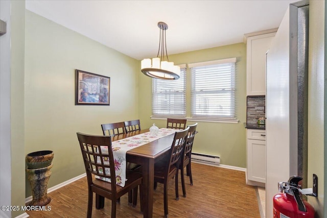 dining area with light wood-type flooring, a notable chandelier, baseboard heating, and baseboards