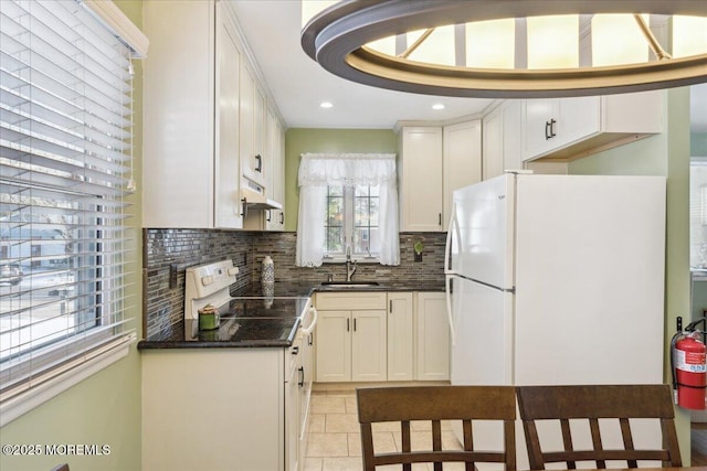 kitchen with a sink, under cabinet range hood, tasteful backsplash, white cabinets, and electric range