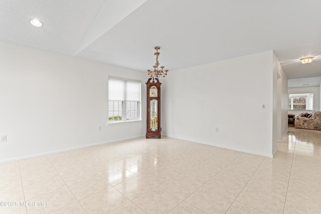 empty room featuring a chandelier, light tile patterned floors, and baseboards