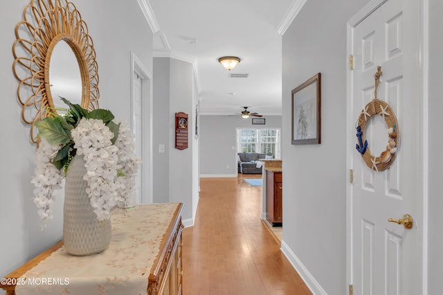 corridor with crown molding, baseboards, visible vents, and light wood-type flooring