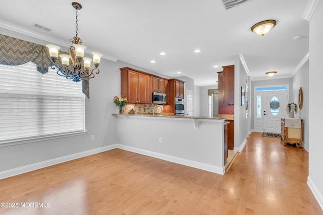kitchen featuring a chandelier, a peninsula, crown molding, light wood-style floors, and appliances with stainless steel finishes