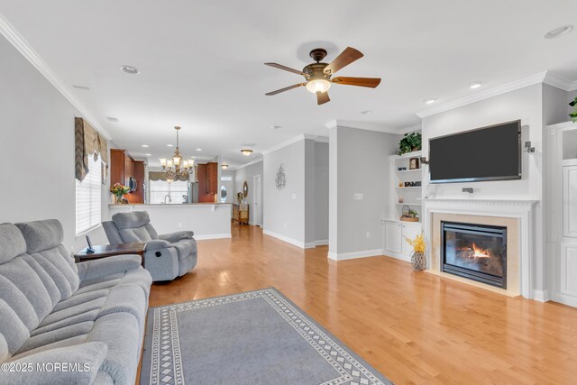 living room featuring baseboards, recessed lighting, ceiling fan with notable chandelier, light wood-style flooring, and a glass covered fireplace