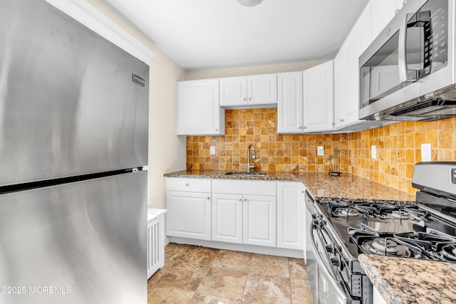 kitchen featuring tasteful backsplash, white cabinetry, appliances with stainless steel finishes, light stone counters, and a sink
