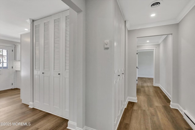hallway with recessed lighting, crown molding, visible vents, a baseboard radiator, and wood finished floors