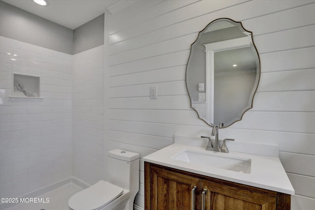 bathroom featuring toilet, tiled shower, and vanity