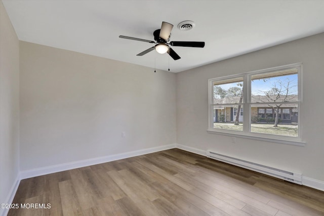 empty room featuring a ceiling fan, visible vents, wood finished floors, a baseboard heating unit, and baseboards