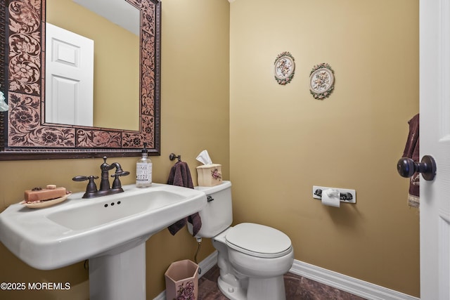 half bath with toilet, baseboards, and a sink