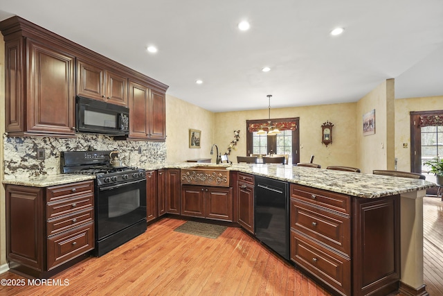 kitchen featuring light wood-type flooring, a peninsula, light stone counters, and black appliances