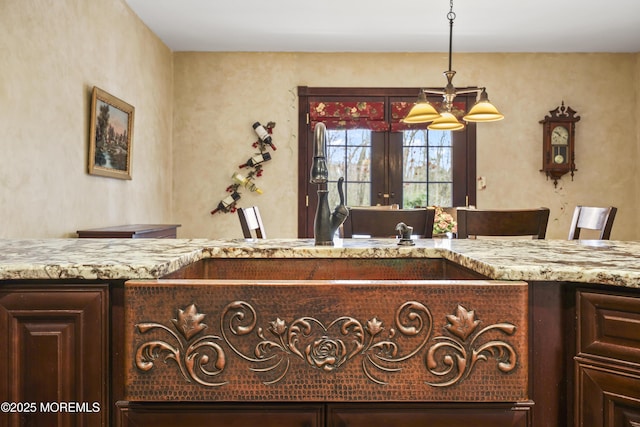 interior space with a chandelier, dark brown cabinetry, light stone countertops, and hanging light fixtures